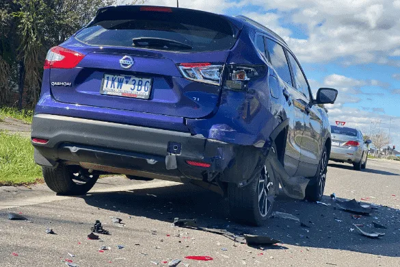 A blue SUV is parked on the roadside with visible rear-end damage, suggesting the need for a hit and run accident lawyer. Debris is scattered on the ground, while another vehicle is seen in the distance.