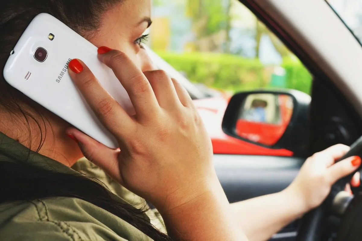 A person with orange-painted nails holds a Samsung smartphone to their ear while driving a car, illustrating a scenario where a Distracted Driving Lawyer may be needed.