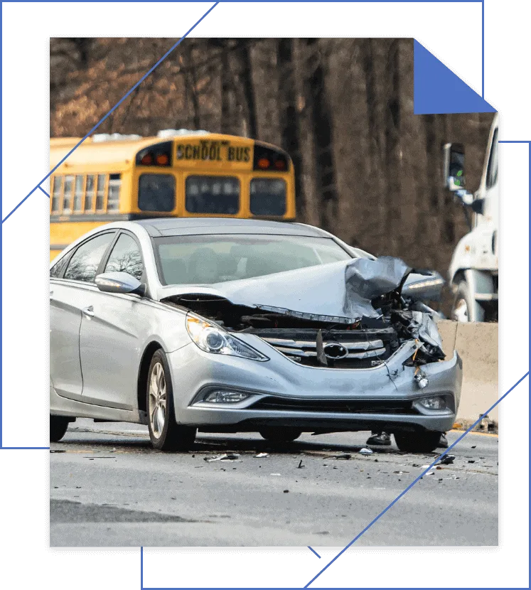 Damaged silver sedan on the road after a collision, with a yellow school bus visible in the background.