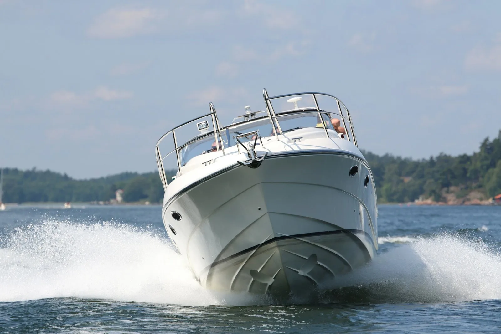 A sleek white speedboat zips across the water's surface, slicing through waves with precision. Trees and distant shorelines form a serene backdrop to its exhilarating journey.