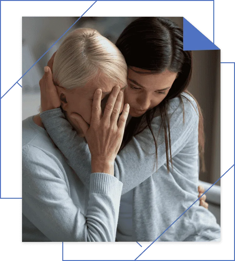 An older woman covers her face in grief while a younger woman embraces her comfortingly.