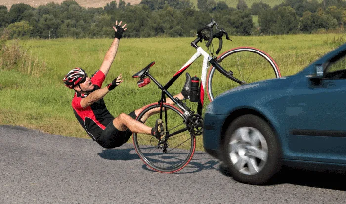 Cyclist in red and black gear involved in a bike accident as a car passes by on a rural Michigan road.