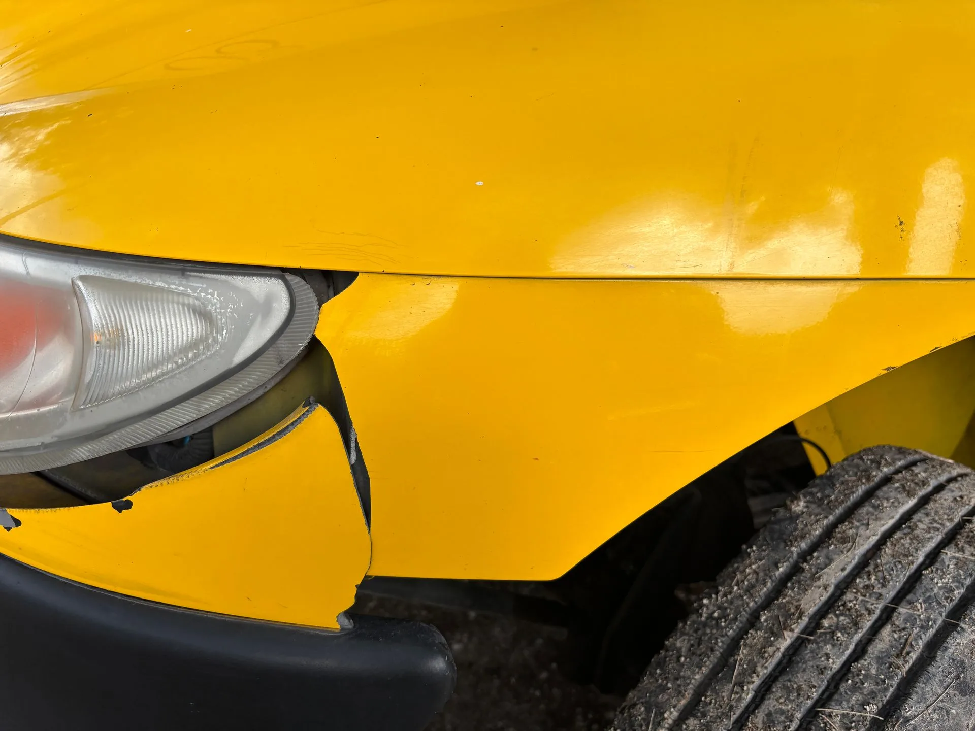 Close-up of a damaged front bumper and headlight on a yellow car