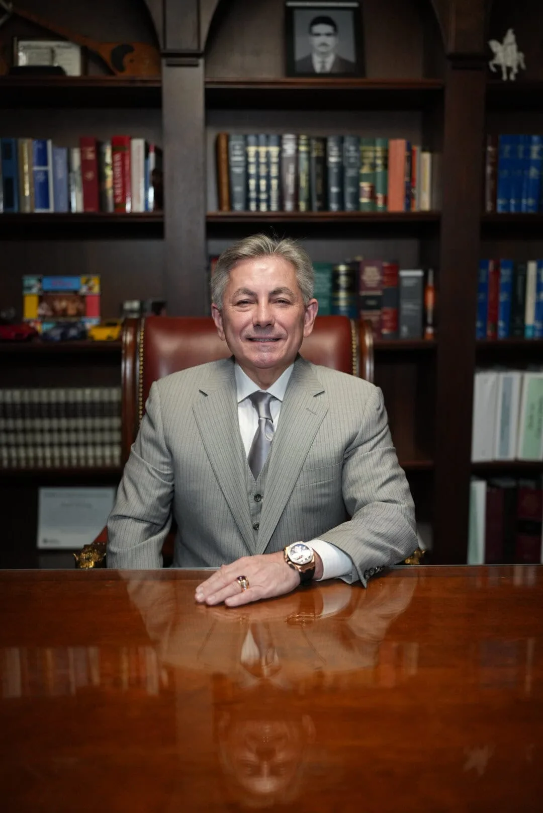 Joseph Dedvukaj seated at his desk in the firm's Bloomfield Hills office, in front of a bookshelf of legal volumes