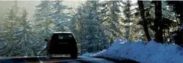 A car glides carefully along a snow-covered road, surrounded by snow-laden trees under a clear sky, reminding us of winter car accident statistics and the importance of cautious driving in cold weather conditions.