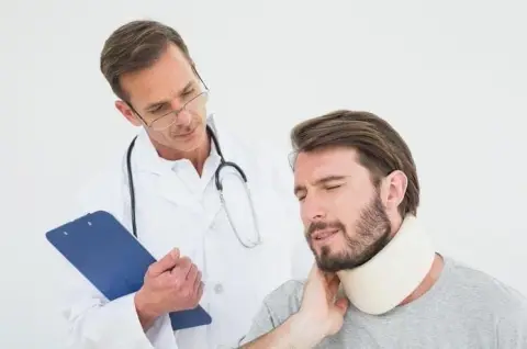 A doctor with a clipboard conducts an Independent Medical Examination on a man wearing a neck brace, who is gently touching his neck.