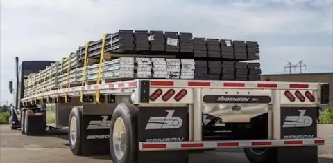 A flatbed truck loaded with stacked metal beams secured with straps is parked on a paved surface, ready for inspection by flatbed truck accident lawyers offering free consultation services.