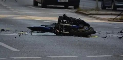 A motorcycle lies on its side in the middle of a road, appearing damaged after an accident—a stark reminder of the importance of motorcycle safety. Debris is scattered around the site.