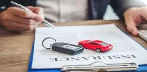 A person holds a pen over an insurance document, accompanied by a car key and a small red toy car. This scene reflects the typical process when dealing with Michigan's no-fault insurance regulations.