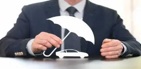 A person in a suit holds a cutout of a white umbrella over a white car model on a table, symbolizing Michigan auto insurance and protection for savvy auto insurance buyers.