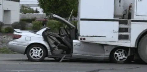 A silver car is partially lodged under the rear of a large white truck on a street, with significant front-end damage visible from the accident, highlighting the severity of the car underride incident.