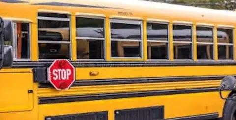 A yellow school bus with an extended stop sign is parked in Sterling Heights, Michigan, emphasizing safety for student loading and unloading. Within the Utica Schools district, stringent measures ensure every aspect of transport avoids the risk posed by a rare drunk bus driver incident.