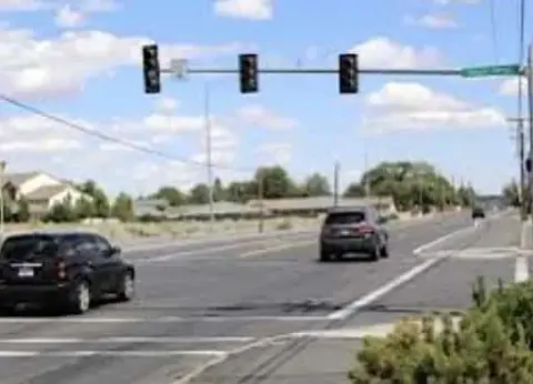 At a quiet Michigan intersection, a few cars wait patiently. The traffic lights shine red against a blue sky punctuated by scattered clouds, leaving drivers to wonder what to do when the signals finally change.