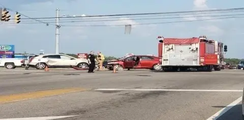At the intersection accident scene, a red car and a white SUV are visibly damaged alongside a fire truck. Emergency personnel attend to those hurt in the wreck, ensuring safety and assessing personal injuries.