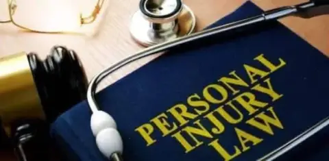 Close-up of a book titled "Personal Injury Law" with a stethoscope, a gavel, and glasses resting on a wooden surface, illustrating the essential tools in navigating the basic stages of a Michigan personal injury lawsuit.