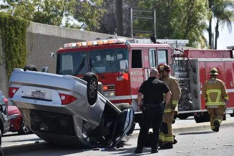 Firefighters and police officers are diligently working at the scene of an overturned car accident, with a fire truck stationed in the background. In such situations, consulting a rollover accident lawyer can be crucial for understanding your rights and seeking justice.
