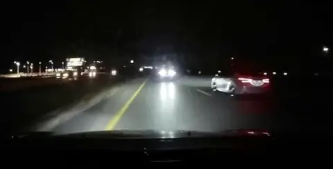 Nighttime highway scene in Michigan with cars driving in opposite directions. The road, illuminated by headlights, has roadside lights visible in the background. Remember safety tips to avoid being a wrong way driver on these bustling roads.