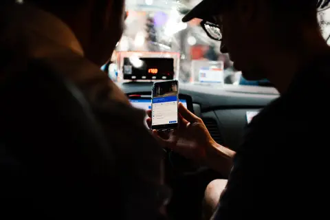 Passengers checking a ride app on a phone inside a car at night