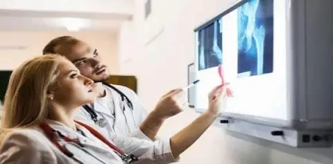 Two doctors examine X-ray images on a lightbox, discussing the findings and possible injuries.