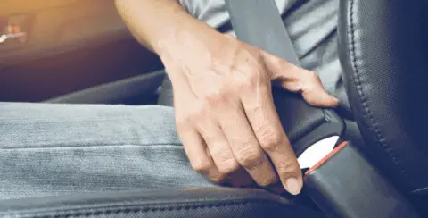 Wearing blue jeans and a grey shirt, the person attentively fastens their seatbelt, ensuring safety on the road and minimizing the risk of injury in case of a car accident.