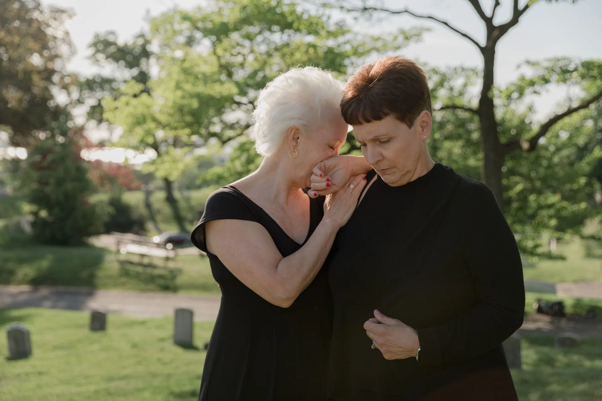 Two women dressed in black comforting each other in a cemetery