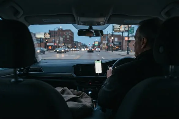 View from the back seat of a rideshare vehicle at dusk with a dashboard navigation phone