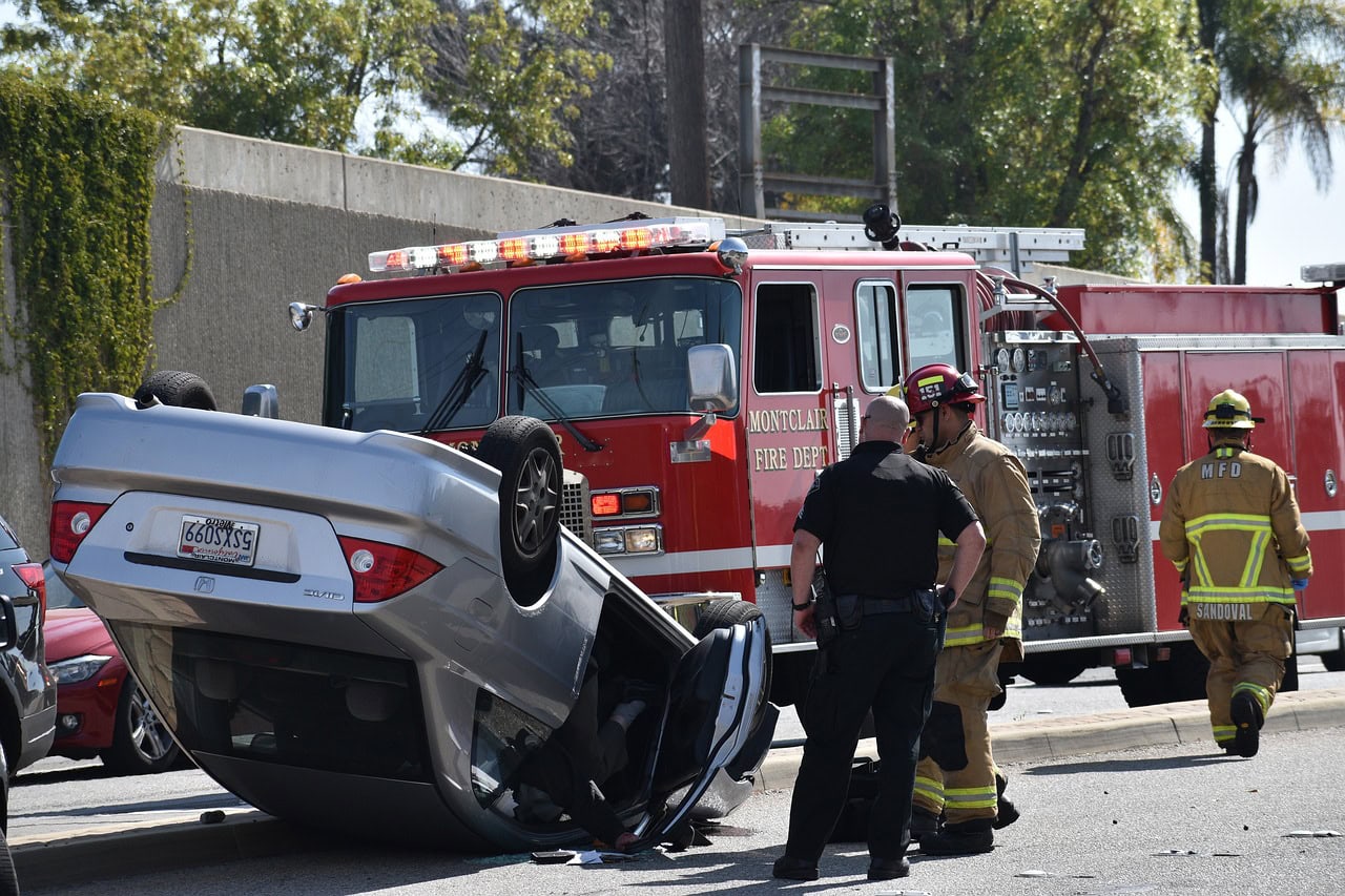 Firefighters and police officers are diligently working at the scene of an overturned car accident, with a fire truck stationed in the background. In such situations, consulting a rollover accident lawyer can be crucial for understanding your rights and seeking justice.