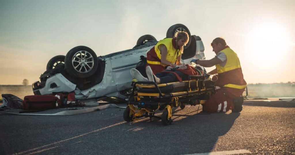 Emergency responders assist an individual on a stretcher beside an overturned car, highlighting the real-life impact behind Michigan Traffic Crash Data.