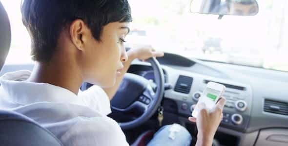 A person is driving a car, contributing to potential auto injuries by glancing at their smartphone.