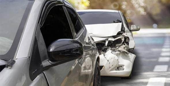 Two cars are involved in a rear-end collision on a road. The front car is silver, while the rear white car shows significant damage to its front. Car accident lawyers can assess such scenarios for any liability issues or defective equipment claims that might arise.