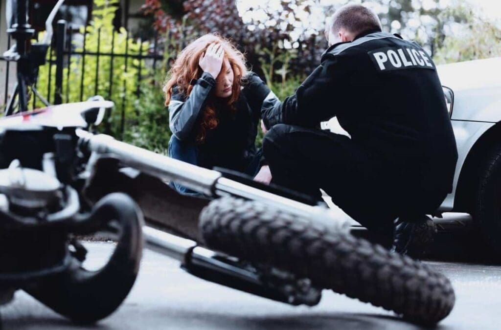 A police officer assists a seated woman near an overturned motorcycle on the street, potentially factoring into a motorcycle accident claim in Michigan.