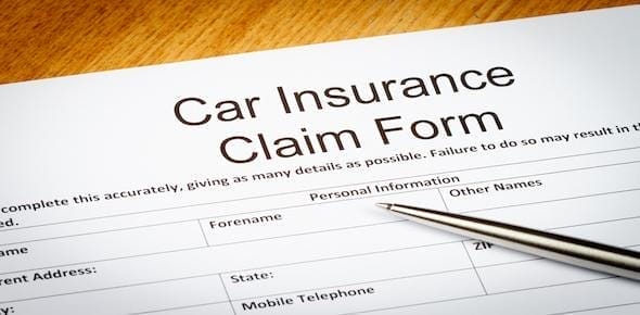 A close-up of a car insurance claim form reveals sections for personal information, including forename and other names, with a pen atop. This form is essential when you deal with an insurance adjuster after an auto accident.