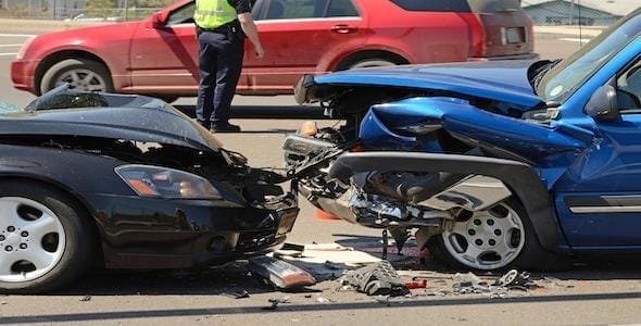 In a dramatic head-on accident, two cars lie damaged on the road, debris strewn across the scene. A person in a reflective vest appears in the background, perhaps gathering details for those who need to know what happened.