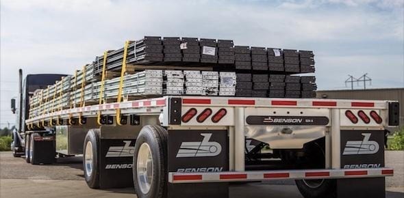 A flatbed truck loaded with stacked metal beams secured with straps is parked on a paved surface, ready for inspection by flatbed truck accident lawyers offering free consultation services.