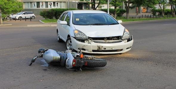 A white car and a motorcycle have collided on a city street, with the motorcycle lying on its side in front of the car. If you're involved in a motorcycle accident, knowing what to do next is crucial, like contacting a lawyer for advice.