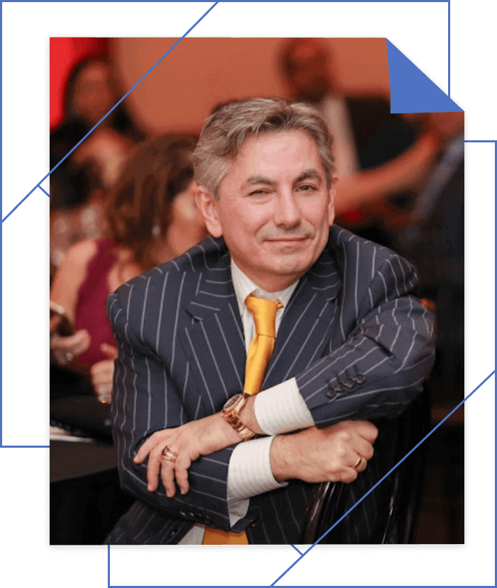 Man in a pinstriped suit and yellow tie sits with folded arms, smiling at an event.