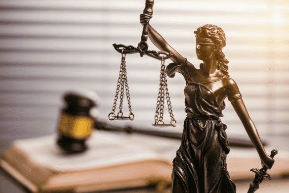 A statue of Lady Justice holding scales, with a judge's gavel and open book in the background, symbolizes fairness and knowledge—much like seeking answers to frequently asked personal injury questions in Michigan.