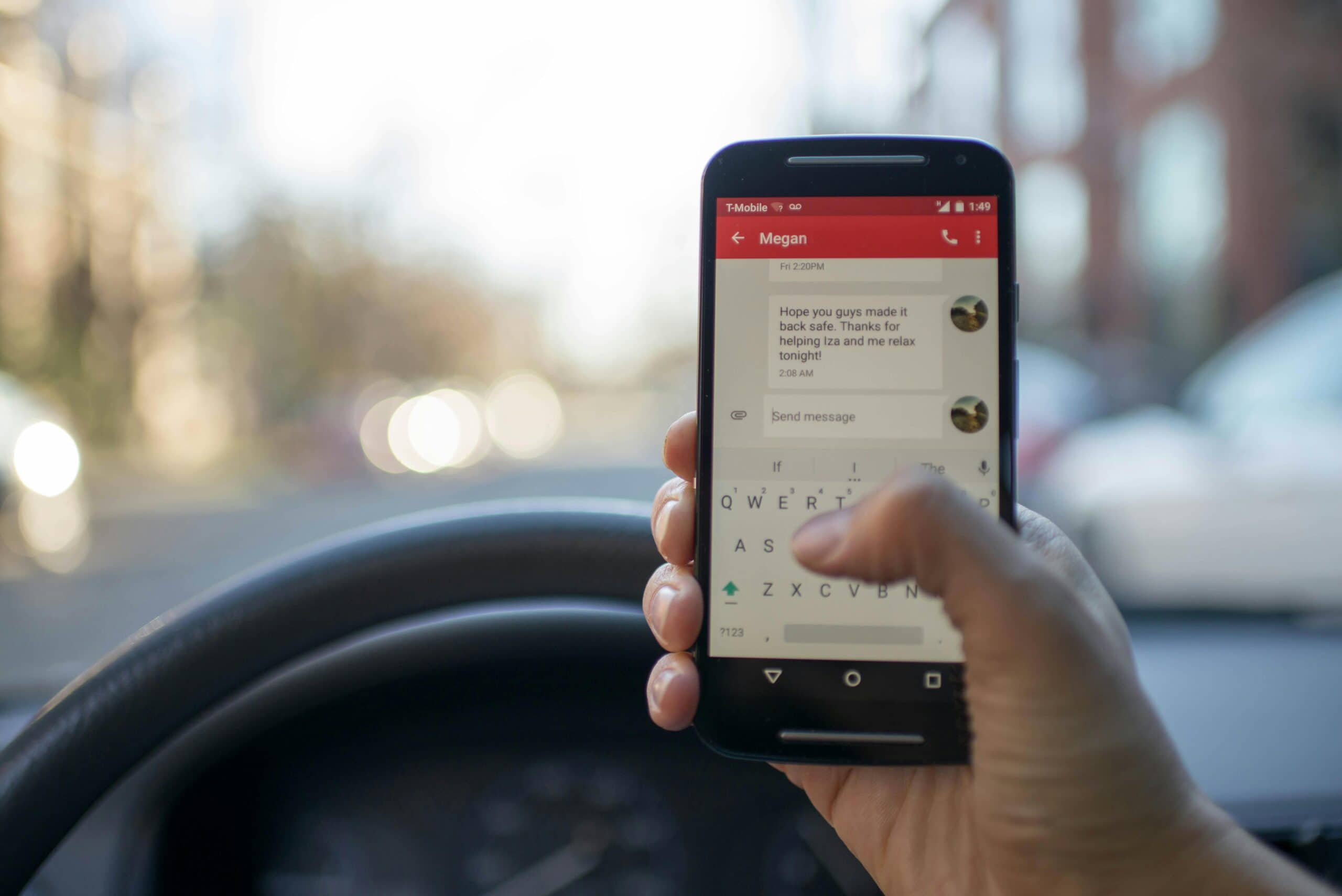 A person texting on a smartphone while sitting behind the steering wheel of a car during daylight, illustrating the risks of a distracted driving accident.