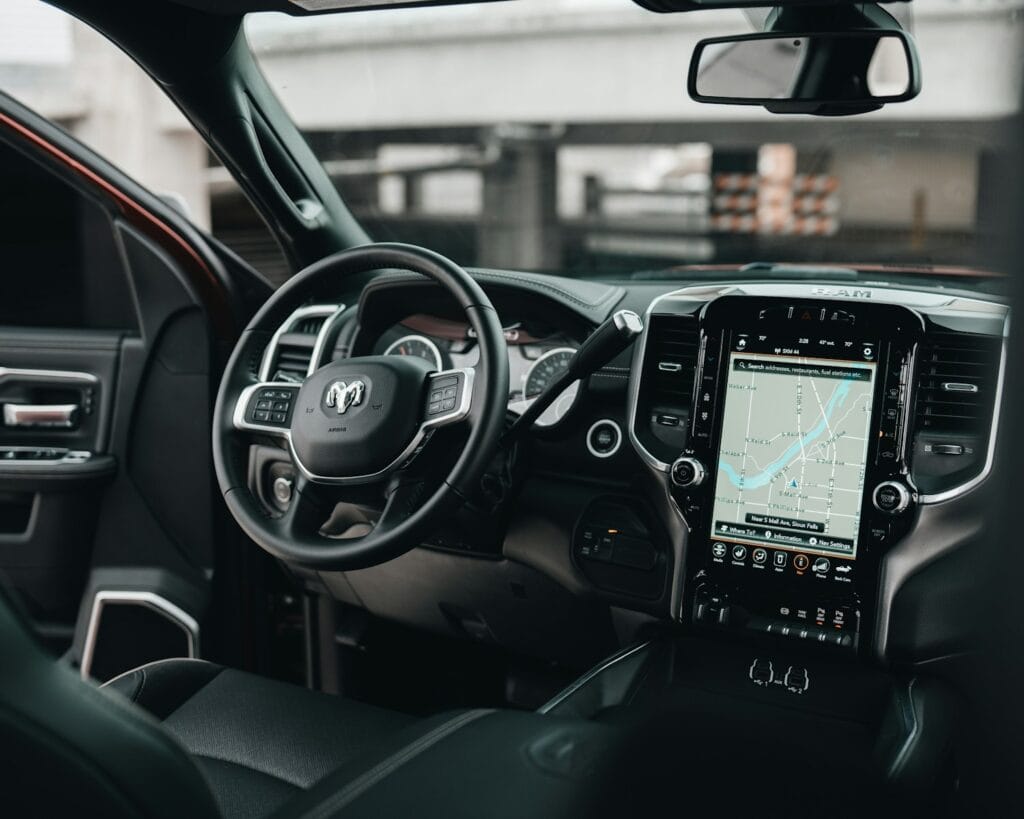 Interior view of a modern pickup truck showing the steering wheel, dashboard, and large central touchscreen display with navigation map—ideal for discussing autonomous vehicle liability or consulting a lawyer after a self-driving car accident in Michigan.