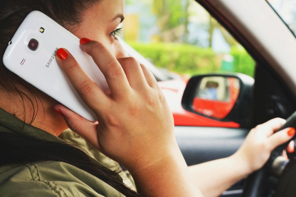 A person with orange-painted nails holds a Samsung smartphone to their ear while driving a car, illustrating a scenario where a Distracted Driving Lawyer may be needed.