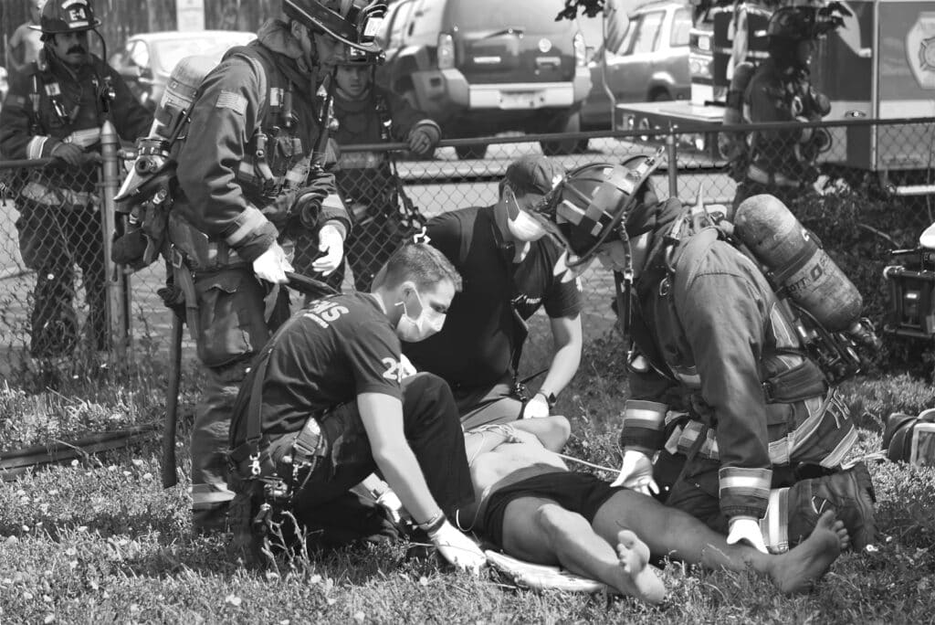 Firefighters and paramedics attend to a person lying on the ground after a pedestrian accident, providing medical assistance in an outdoor emergency scene.