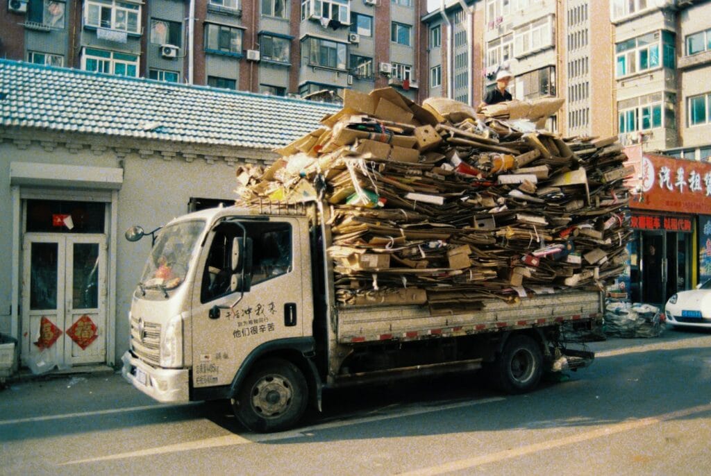 An overloaded truck piled high with cardboard and paper travels down a Michigan city street, risking overloaded truck accidents despite federal weight regulations.