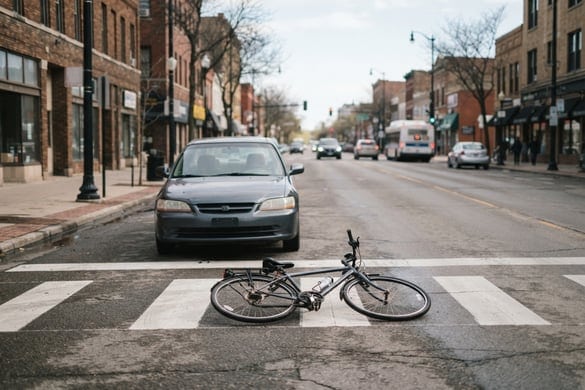 Bicycle lying on a crosswalk in front of a stopped car after a bicycle accident