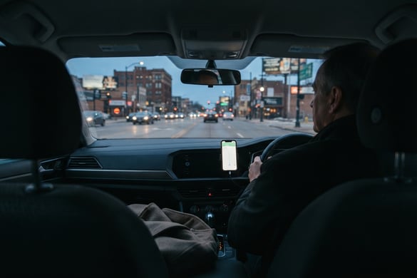 View from the back seat of a rideshare vehicle at dusk with a dashboard navigation phone