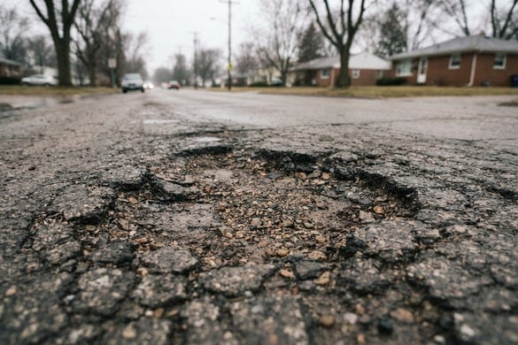 Large pothole and cracked asphalt on a Michigan road, a common road defect hazard